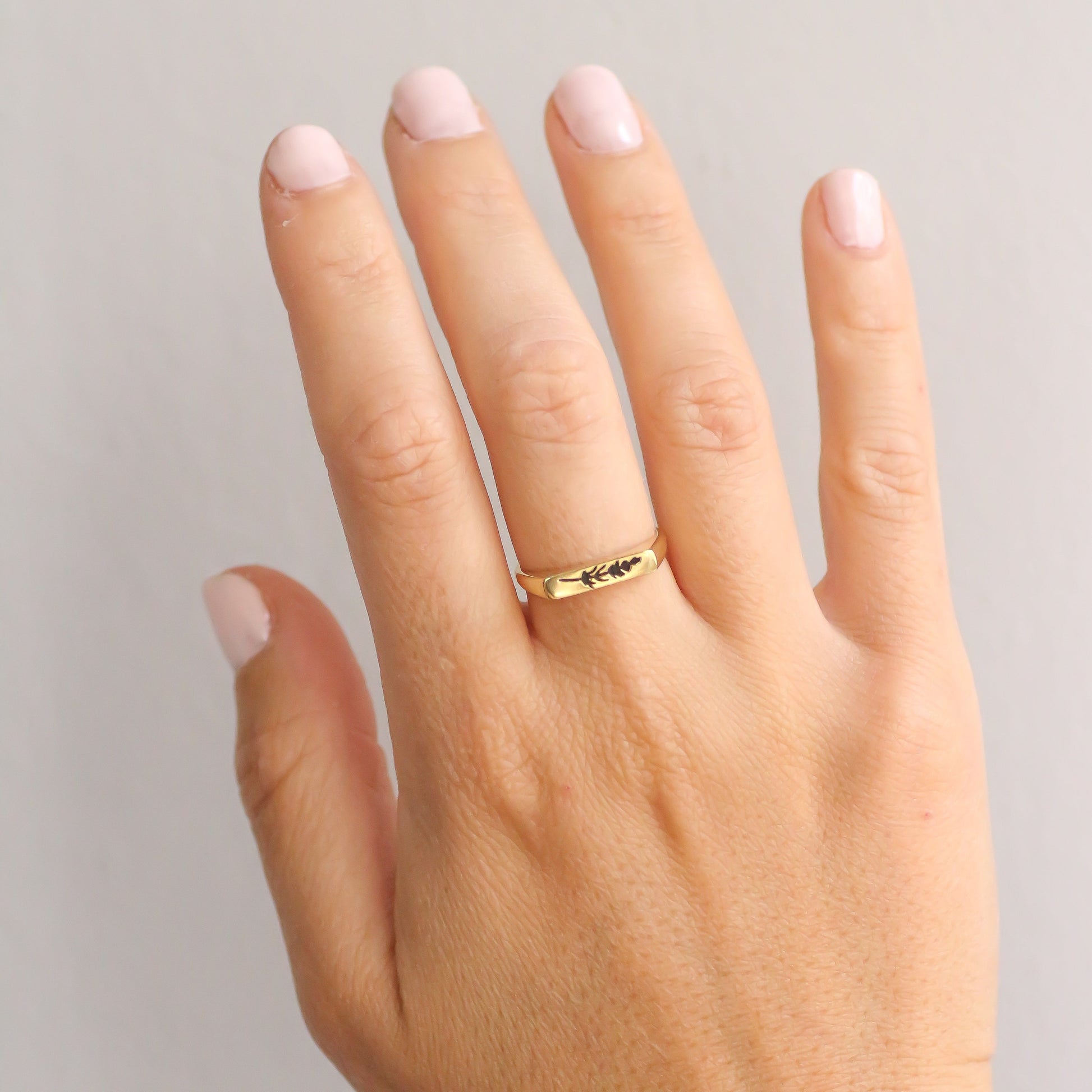 Hand wearing a thin gold signet ring with a lavender engraving